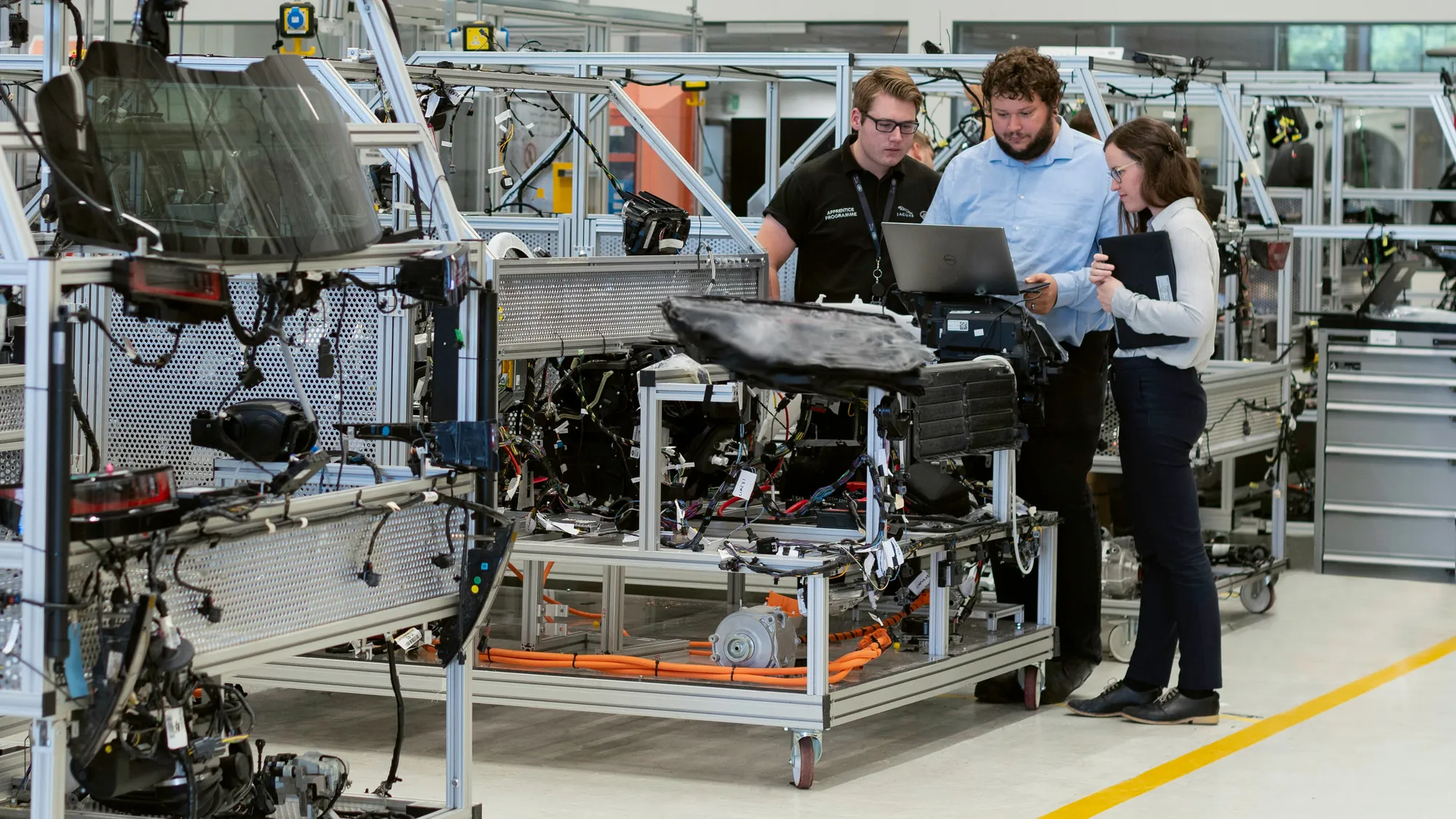 Tre persone osservano dati e attrezzature in un ambiente industriale.